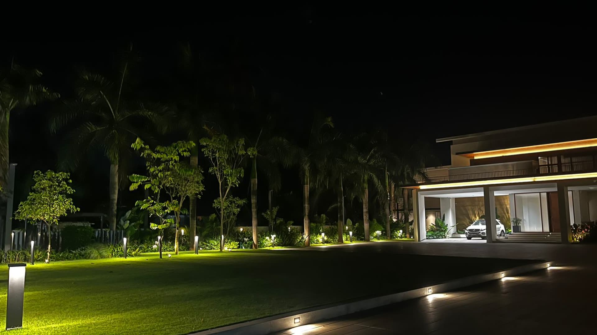 A villa at night with its approach, lawn and facade lit as a single scheme