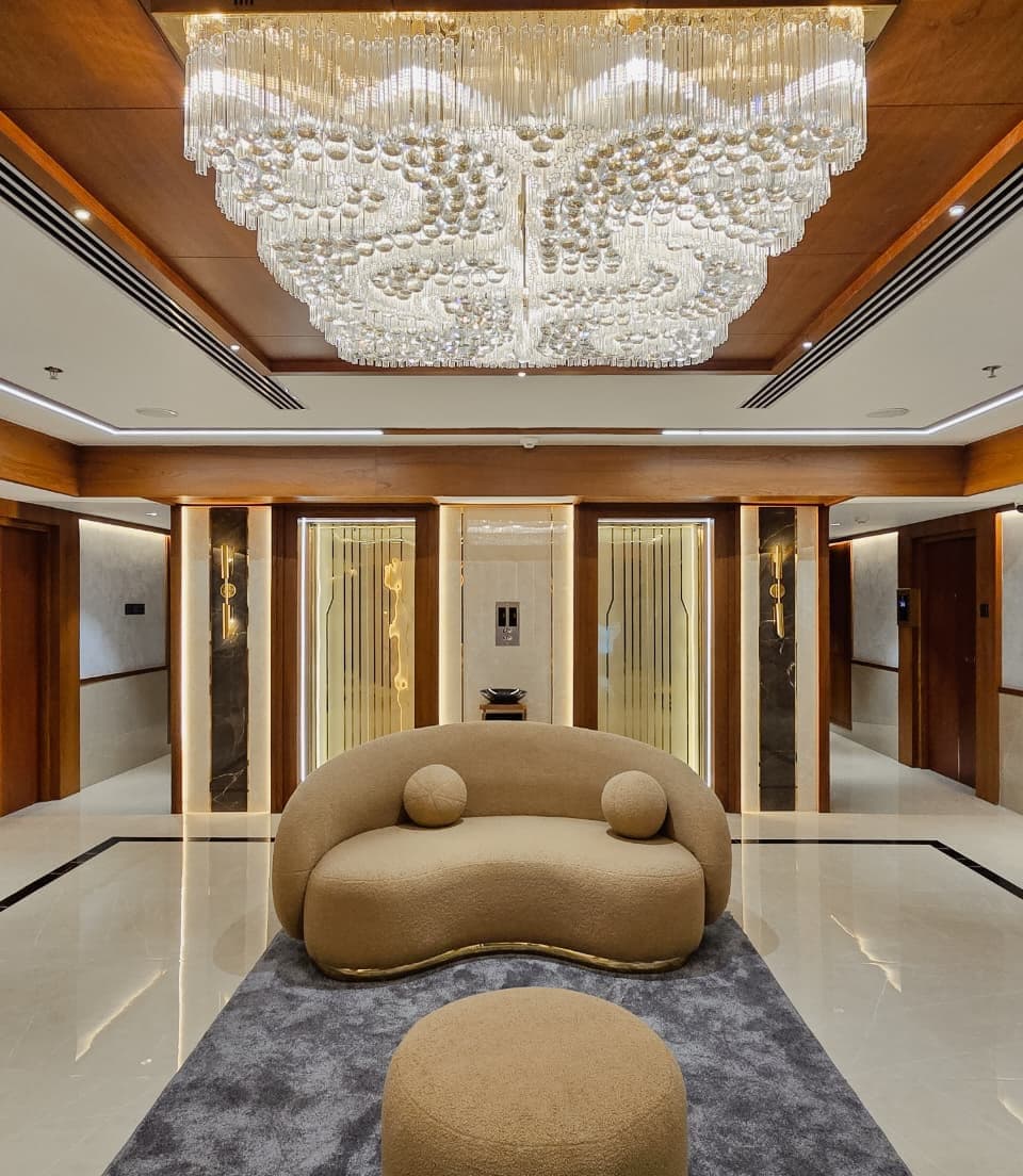 A hotel lift lobby under a wide crystal ceiling fixture, with backlit gold fluted panels