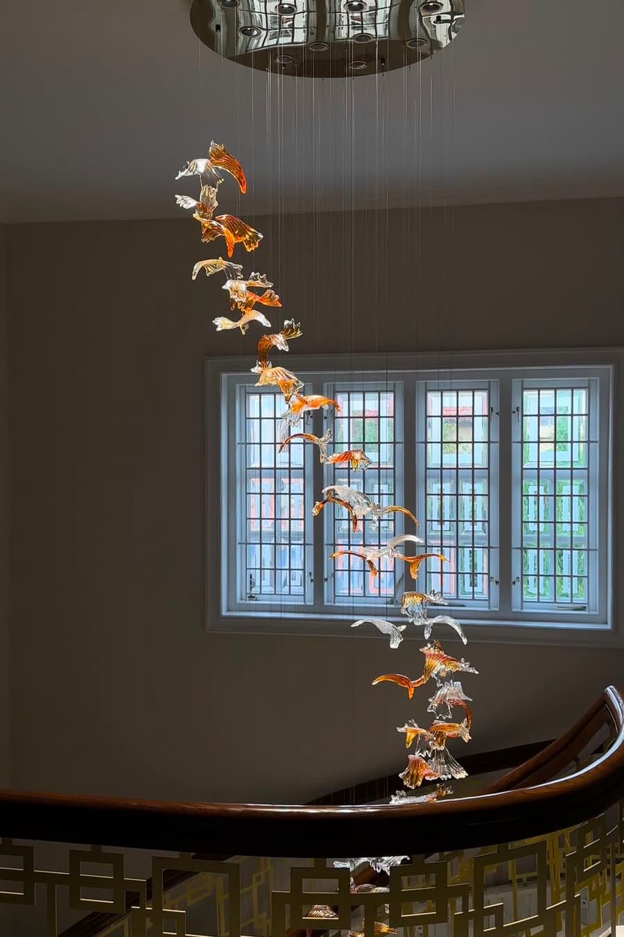 A bespoke glass bird cascade falling past a tall stairwell window