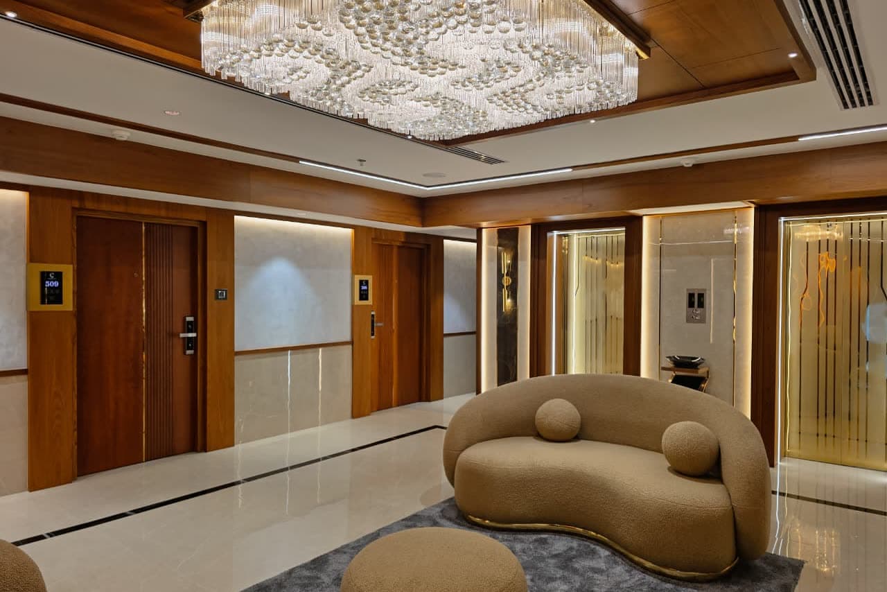 A hotel lift lobby with a wide crystal ceiling fixture and backlit gold panels