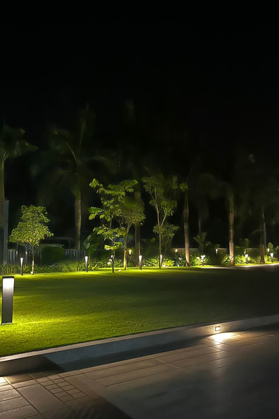 A villa lawn at night lit by bollards and tree uplights